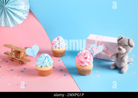 Délicieux cupcakes avec boîte-cadeau, décorations et jouets sur fond de couleur. Concept de parti de révélation de genre Banque D'Images