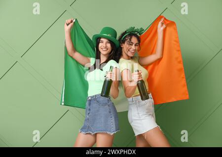 Belles jeunes femmes avec drapeau irlandais et bouteilles de bière sur fond vert. Prog Célébration de la fête de Patrick Banque D'Images