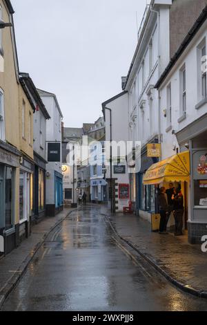 Vue le long d'une rue humide et déserte, avec des gens debout à la boutique de poissons et de puces attendant et les lumières reflétées dans les flaques d'eau. Banque D'Images