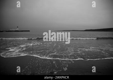 Vagues douces se précipitant sur une plage de sable avec un port et un phare à travers la baie, Scarborough South Bay, North Yorkshire, Angleterre. Banque D'Images