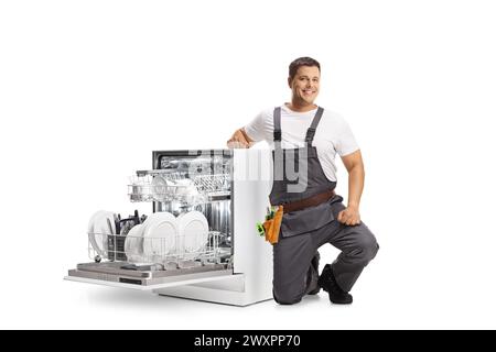 Réparateur agenouillé à côté d'un lave-vaisselle et souriant isolé sur fond blanc Banque D'Images