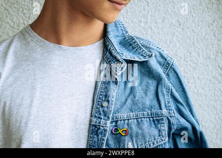 Adolescent garçon avec autisme Infinity symbole arc-en-ciel signe broche métallique sur veste en denim. Journée mondiale de sensibilisation à l'autisme, mouvement pour les droits de l'autisme Banque D'Images