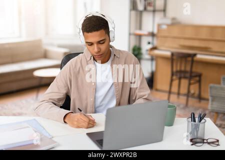 Homme avec écouteurs écrivant des notes au bureau Banque D'Images