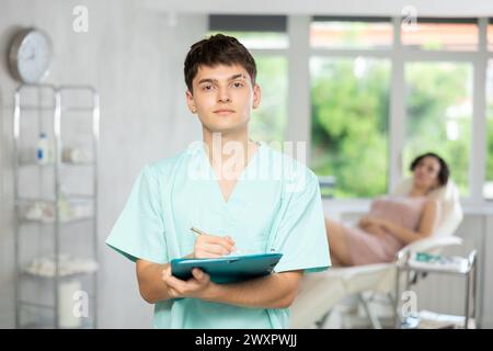 Jeune homme médecin posant dans le cabinet du médecin avec le document en main Banque D'Images