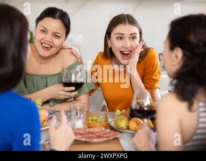 Des femmes heureuses se sont rassemblées autour d’une table festive, participant à des discussions animées et profitant des délices du vin Banque D'Images
