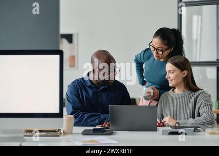 Groupe de trois gais gestionnaires masculins et féminins ethniquement diversifiés travaillant sur le projet dans un bureau moderne, espace de copie Banque D'Images