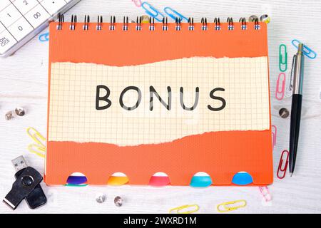 Mot anglais Bonus écrit sur un morceau de papier sur un carnet orange Banque D'Images