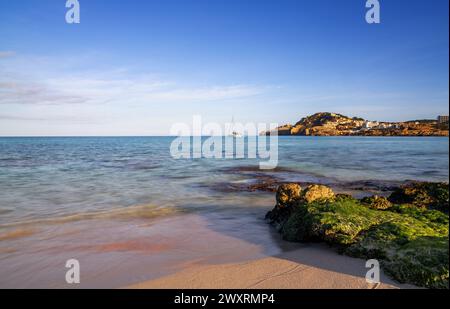 Une vue sur la baie idyllique et la plage de Cala Agulla dans l'est de Majorque avec un voilier au premier plan Banque D'Images