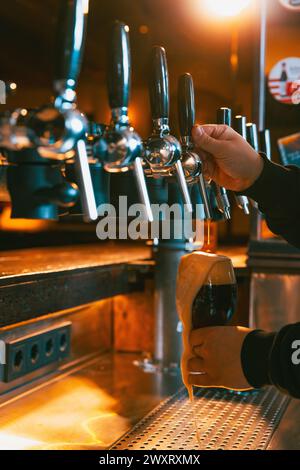 Bière brune artisanale, lager, froide et mousseuse versée dans le verre à pied par le barman au bar traditionnel. Servir de la bière artisanale du robinet. Concept d'Oktoberfest. Banque D'Images