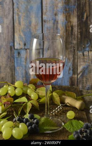 Verre de vin rouge avec des raisins verts et tire-bouchon sur fond en bois. Banque D'Images