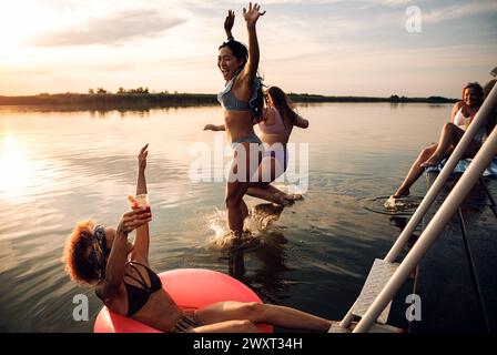 Groupe d'amies profitant d'une journée d'été sautant au lac. Banque D'Images