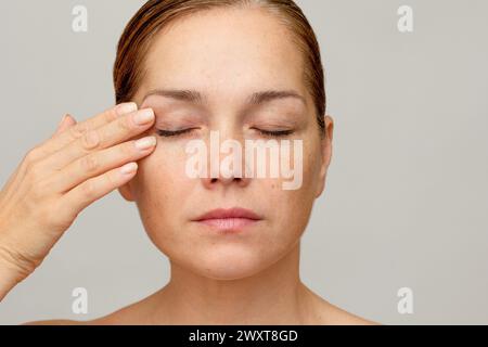 Femme caucasienne d'âge moyen des années 40 avec les yeux fermés tenant le doigt sur la paupière Banque D'Images