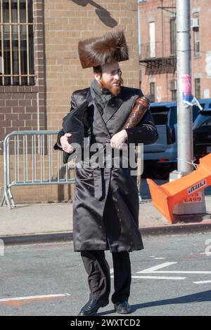 Un homme juif orthodoxe revient du temple sur Pourim portant un chapeau de fourrure shtreimel et portant un sac tallis et une megillah. À Brooklyn, New York. Banque D'Images