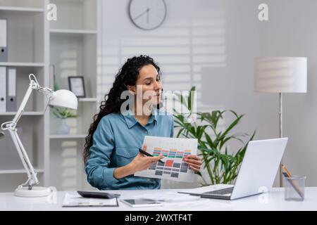 Femme hispanique professionnelle examine des documents dans un bureau à domicile bien organisé, travaillant sur un nouveau projet avec son ordinateur portable. Banque D'Images