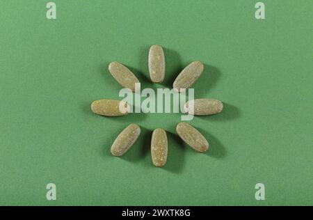 Pilules fines herbes et vitamine Green posées librement sur fond vert Banque D'Images
