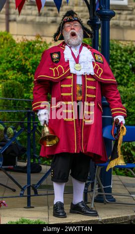 Crier de la ville masculine (livrée de crieur tressé rouge coloré) proclamant une annonce et faisant une proclamation publique bruyante - Ilkley, West Yorkshire Angleterre Royaume-Uni. Banque D'Images