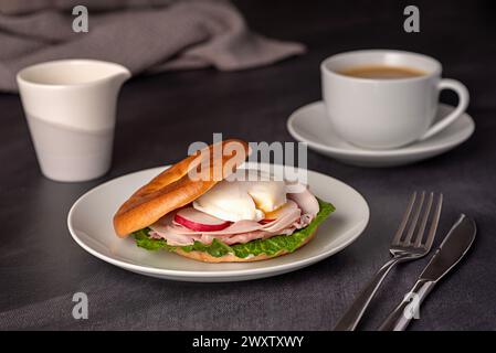 Photographie culinaire de bagel avec oeuf poché, radis, bacon, jambon, café, cappuccino, latte ; laitue romaine ; sandwich ; matin; tranché ; petit déjeuner ; brun Banque D'Images