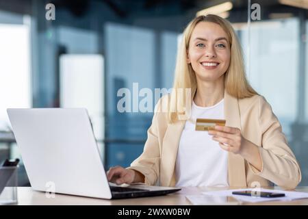 Femme d'affaires confiante utilisant un ordinateur portable et une carte de crédit pour les achats en ligne dans un cadre de bureau moderne. Banque D'Images