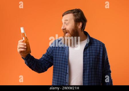 Joyeux homme barbu criant tient bouteille de bière, fond orange Banque D'Images