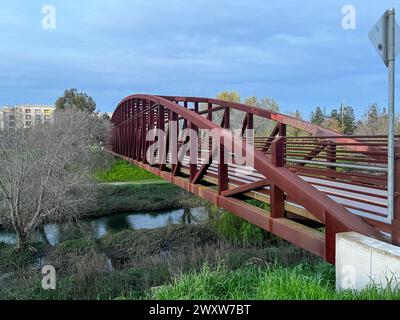 Un pont rouge enjambe un champ vert luxuriant avec des structures en arrière-plan Banque D'Images