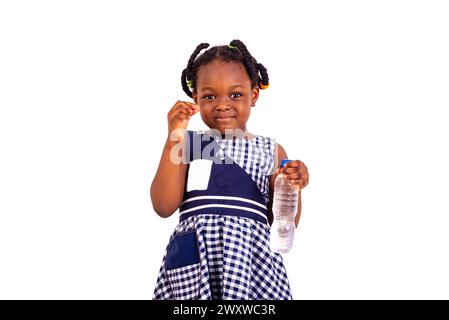 mignonne petite fille vêtue de vêtements d'école tenant la bouteille d'eau en plastique souriant. Banque D'Images