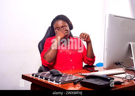 charmante femme d'affaires dans des verres assis au bureau travaillant avec l'ordinateur se sentant épuisé. Banque D'Images