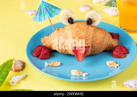 Croissant en forme de crabe avec fraise et banane sur plaque bleue sur fond jaune - nourriture amusante pour les enfants Banque D'Images