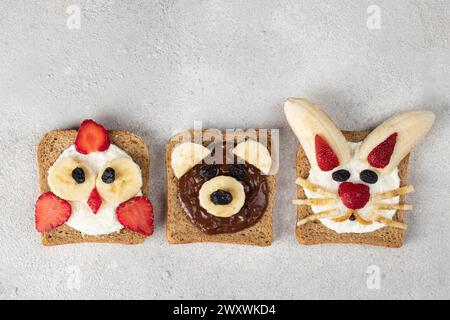 Toasts sucrés pour enfants en forme de poussin, ours et lapin, avec fraises, banane, fromage à la crème, flocons de chocolat et de noix de coco sur fond gris Banque D'Images