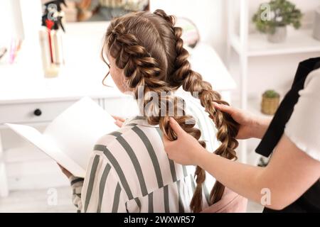 Coiffeur professionnel tressant les cheveux du client dans le salon Banque D'Images