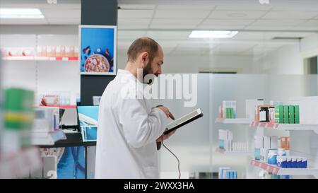 Le commis à la pharmacie inspecte l'approvisionnement en produits pharmaceutiques dans les allées, scannant les boîtes contenant des produits de santé et des traitements dans le centre médical. Le membre du personnel compte les médicaments à l'aide d'une tablette et d'un scanner. Banque D'Images