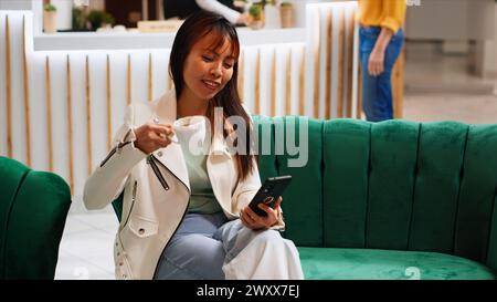 Personne moderne profitant du wifi gratuit dans le hall, en utilisant un smartphone pour passer le temps avant de passer par le processus d'enregistrement. Femme asiatique défilant sur les applications de médias sociaux, concept de tourisme. Banque D'Images