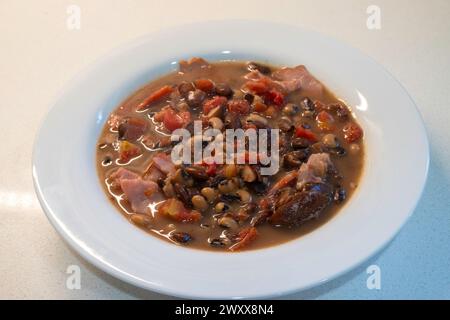 Bol maison de soupe de hamac et de haricots avec tomates servi dans un bol blanc sur fond blanc. Banque D'Images