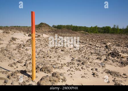 Piquet d'arpenteur en bois peint en rouge et orange ou marqueur dans un sol sablonneux indiquant une ligne de démarcation sur un chantier de construction au printemps, Québec, Canada Banque D'Images