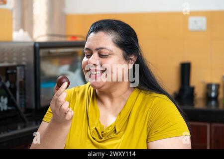 Grosse femme indienne en surpoids s'excitant tenant un morceau de gulab jamun à la maison. Manger malsain, concept d'envie. Banque D'Images