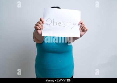 Femme indienne grasse en surpoids tenant le papier blanc écrit obésité. isolé sur fond blanc. Taille plus femelle. Concept de problème de surpoids. Banque D'Images