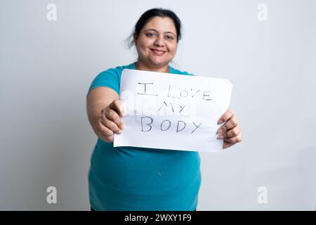 Grosse femme indienne en surpoids tenant du papier blanc écrit j'aime mon corps. isolé sur fond blanc. Taille plus femelle. concept d'amour de soi. Banque D'Images