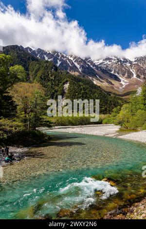 Randonneurs à côté d'une rivière claire avec des montagnes enneigées en arrière-plan sous un ciel bleu Banque D'Images