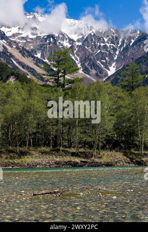 Randonneurs près d'une rivière claire en face d'énormes montagnes enneigées (chaîne Hotaka) Banque D'Images