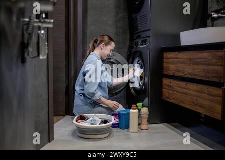 Femme assis devant une machine à laver chargeant des vêtements sales, serviettes pour laver des vêtements colorés Banque D'Images