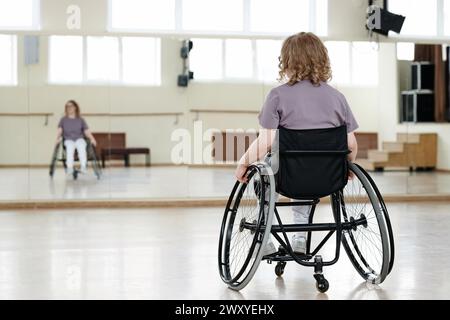 Vue arrière à mise au point sélective d'une jeune femme handicapée méconnaissable en fauteuil roulant pratiquant la danse Banque D'Images