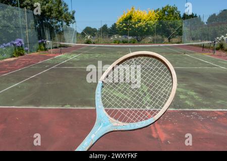 Vieille raquette de tennis en bois avec court de tennis négligé en arrière-plan, Bairnsdale, Victoria, Australie Banque D'Images