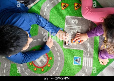 Au-dessus de deux enfants, un garçon et une fille, s'engagent dans un jeu imaginatif avec de petites voitures jouets sur un tapis de jeu vibrant Banque D'Images