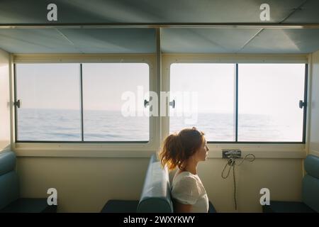 Une femme contemplative regarde par la fenêtre la mer de l'intérieur d'une cabane ensoleillée Banque D'Images