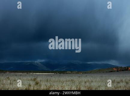 Des nuages sombres et inquiétants planent au-dessus d'une chaîne de montagnes paisible, projetant une ombre sur le paisible champ ouvert en contrebas Banque D'Images