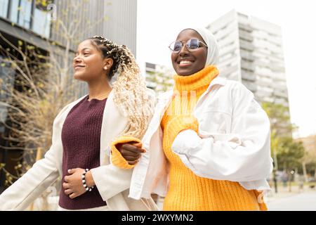 D'en bas, deux femmes afro-américaines multiethniques marchent ensemble dans un cadre urbain, mettant en valeur la camaraderie et la beauté diversifiée. Banque D'Images