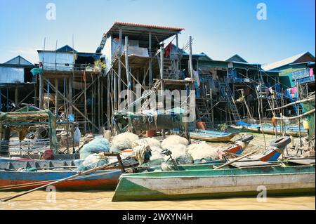 Maisons traditionnelles sur pilotis au-dessus de l'eau avec des bateaux amarrés et des filets de pêche dans un village de pêcheurs d'Asie du Sud-est sous un ciel bleu Banque D'Images