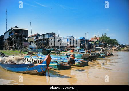 Des maisons sur pilotis s'élèvent au-dessus de l'eau à côté de bateaux traditionnels amarrés dans un village flottant sous un ciel bleu Banque D'Images