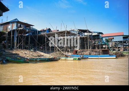 Maisons en bois sur pilotis surplombant une rivière boueuse avec des bateaux traditionnels amarrés le long de la rive sous un ciel bleu clair Banque D'Images