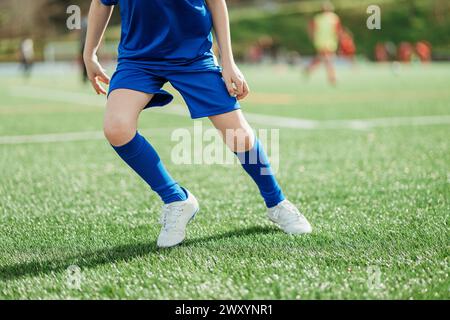 Une photo détaillée se concentre sur les jambes d'un joueur de football en tenue bleue contre un terrain herbeux Banque D'Images