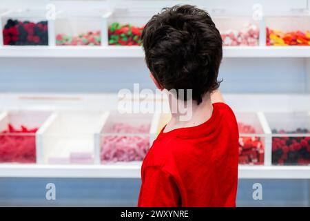 Une personne dans une chemise rouge est vue de derrière, regardant une variété de bonbons colorés affichés dans un magasin Banque D'Images